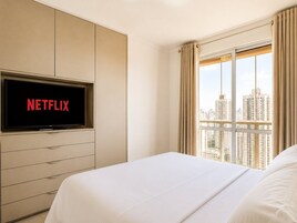 Quarto de hotel com cama, televisão na parede e janela com cortinas.