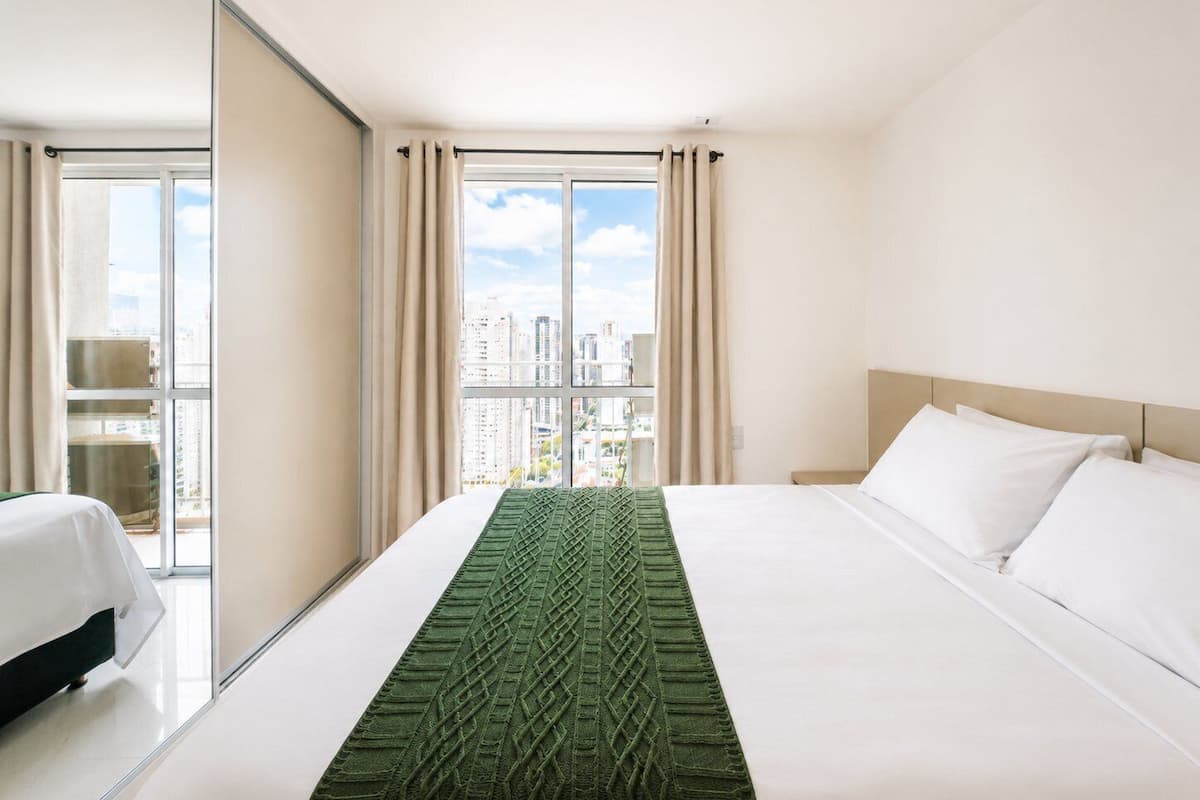 Una habitación de hotel con cama, ventana con cortinas y vistas a edificios.