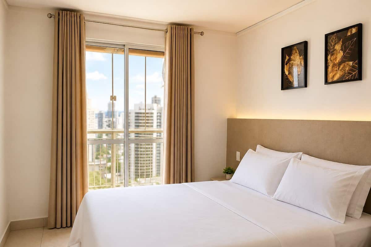 Habitación de hotel con una cama grande, cortinas, vistas de la ciudad y dos cuadros en la pared.