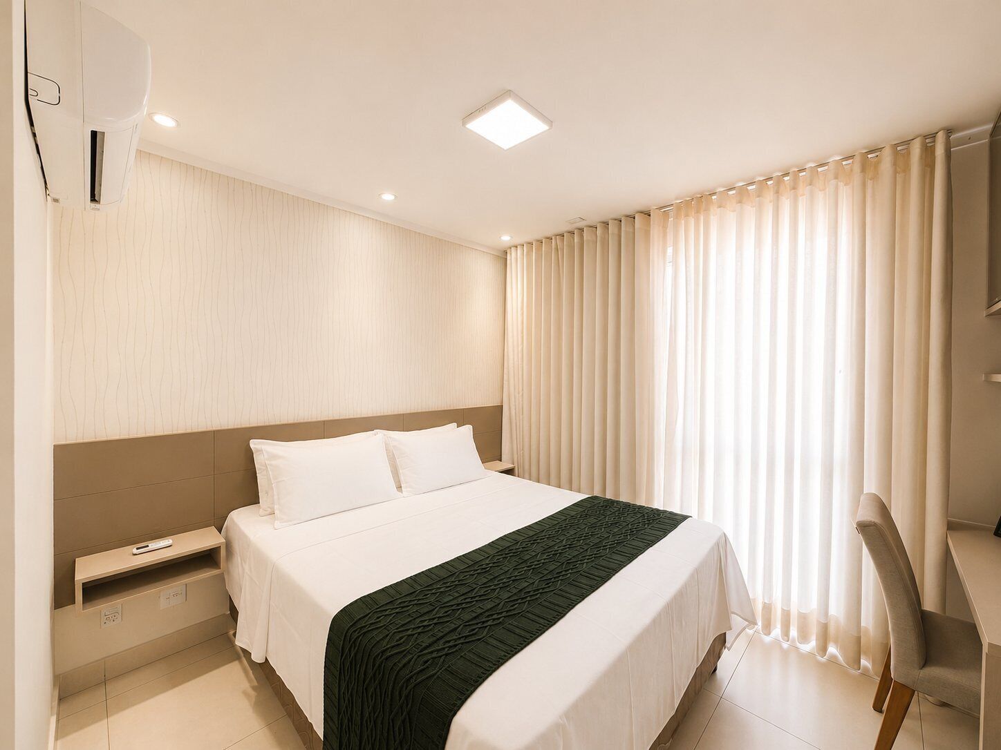 A hotel room with a bed, a desk, a chair, a TV, and a window with curtains.