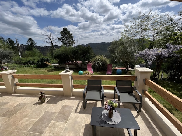 Un patio al aire libre con vistas a montañas, una cerca de madera y una mesa con sillas.