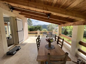 A covered patio with a wooden table, chairs, and a view of the outdoors.