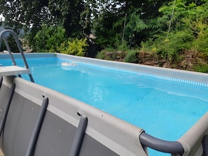 An outdoor swimming pool with a ladder, surrounded by lush greenery.