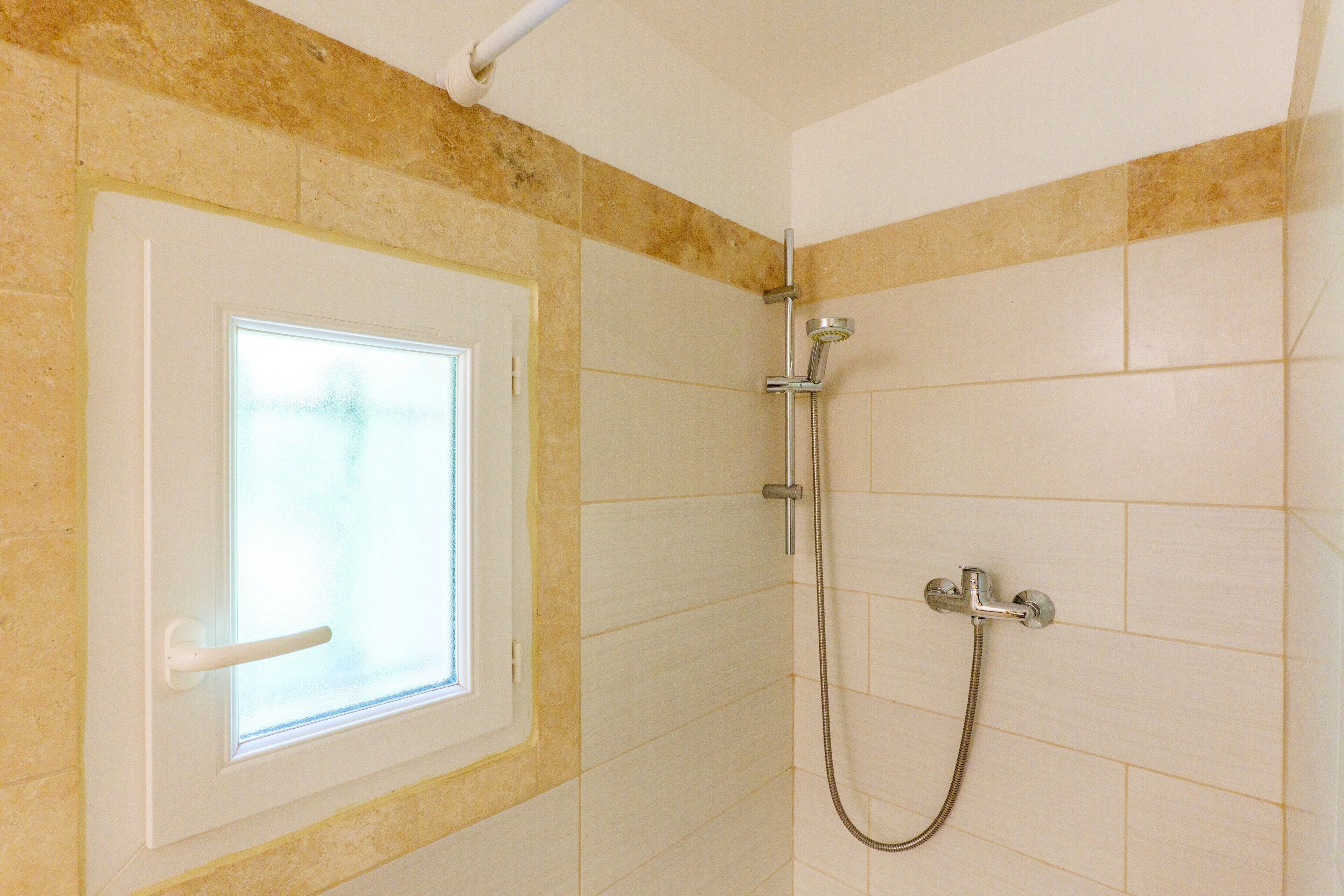 Un baño con ducha, ventana y paredes con azulejos.