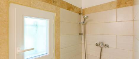 Un baño con ducha, ventana y paredes con azulejos.