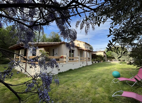 A house with a balcony, a lawn, and a tennis court.