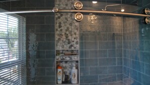 A shower area with a glass door, a metal handle, and a shelf with toiletries.