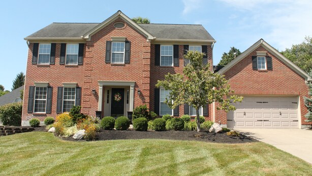A two-story brick house with a front porch, a garage, and a well-maintained lawn.