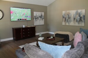 A living room with a flat-screen TV, a dark wooden cabinet, a coffee table, a sofa, and two abstract paintings on the wall. - Peaceful 4-bedroom house with AC in lovely Loveland (Loveland)