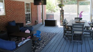 A covered patio with a brick wall, outdoor furniture, a flat-screen TV, and a view of a garden.