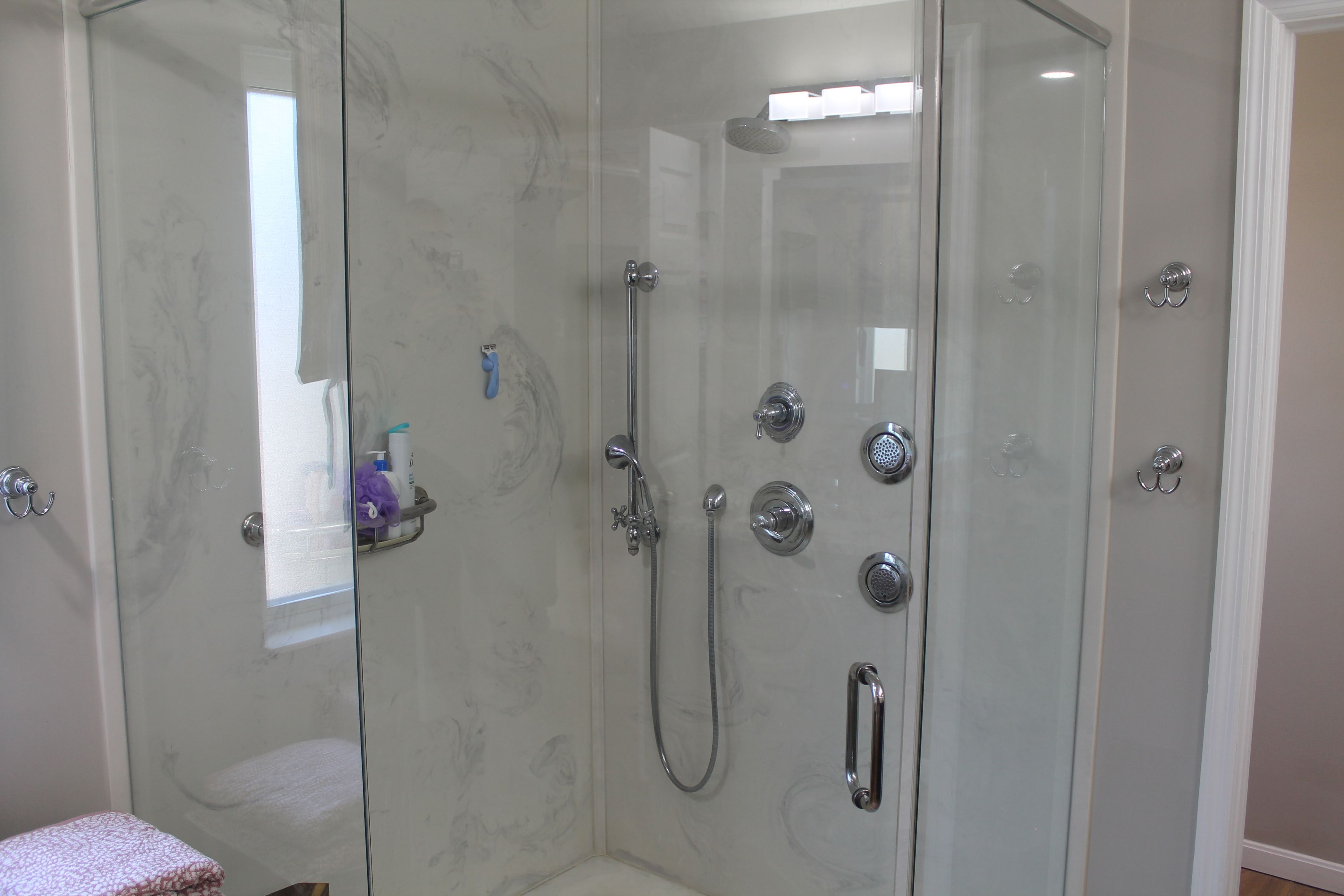 Une cabine de douche fermée par des parois en verre, dotée d’un pommeau de douche à main et d’un robinet mural.