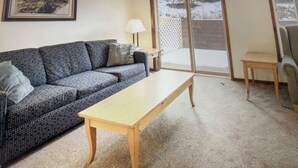 Ein Wohnzimmer mit einer Couch, einem Tisch, einer Lampe und einer Schiebetür zu einem Balkon.