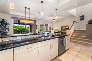 A modern kitchen with a large island, pendant lights, and a view of greenery outside. - Mauna Lani Townhome w/ Golf Course Views Beach Club Access (Kamuela)