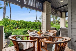 An outdoor patio with a round wooden table set for dining, surrounded by wicker chairs. - Mauna Lani Townhome w/ Golf Course Views Beach Club Access (Kamuela)