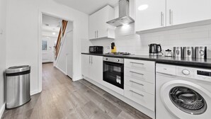 A modern kitchen with white cabinets, a stainless steel range hood, a microwave, a kettle, and a washing machine. - 4 Bed House Close To Gatwick Free Parking (West Sussex)