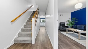 A modern interior with a wooden staircase, a blue accent wall, and a seating area with a plant. - 4 Bed House Close To Gatwick Free Parking (West Sussex)