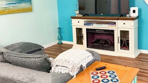Ein Wohnzimmer mit einer Couch, einem Couchtisch mit einem Gesellschaftsspiel, einem Fernseher und einem Kamin.