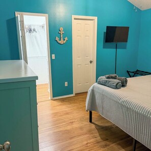 A bedroom with a bed, a dresser, a door, a wall-mounted TV, and a wooden floor.