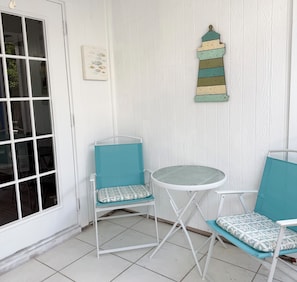 A small patio area with two chairs and a table, a decorative wall piece, and a door with a window.