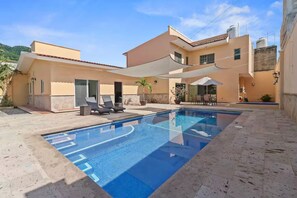 Ein modernes Haus mit Pool, Sitzgelegenheiten im Freien und einer Terrassenfläche.