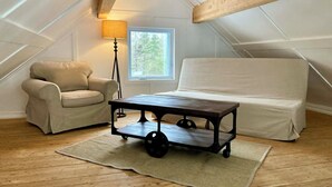 Acogedor dormitorio en el ático con un sofá, una silla, una mesa y una lámpara.