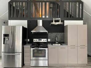 Una cocina moderna con refrigerador, horno y estufa de acero inoxidable, un salpicadero negro y un armario gris.