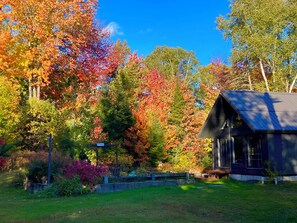 A cabin with a dark roof and a small porch, surrounded by a garden and trees with autumn foliage. - ZEN CHALET located in a peaceful setting not far from the ski slopes (Mille-Isles)