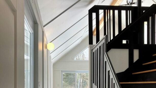 Un interior moderno con una escalera de madera, un comedor con mesa y sillas, y vistas a través de un ventanal grande.