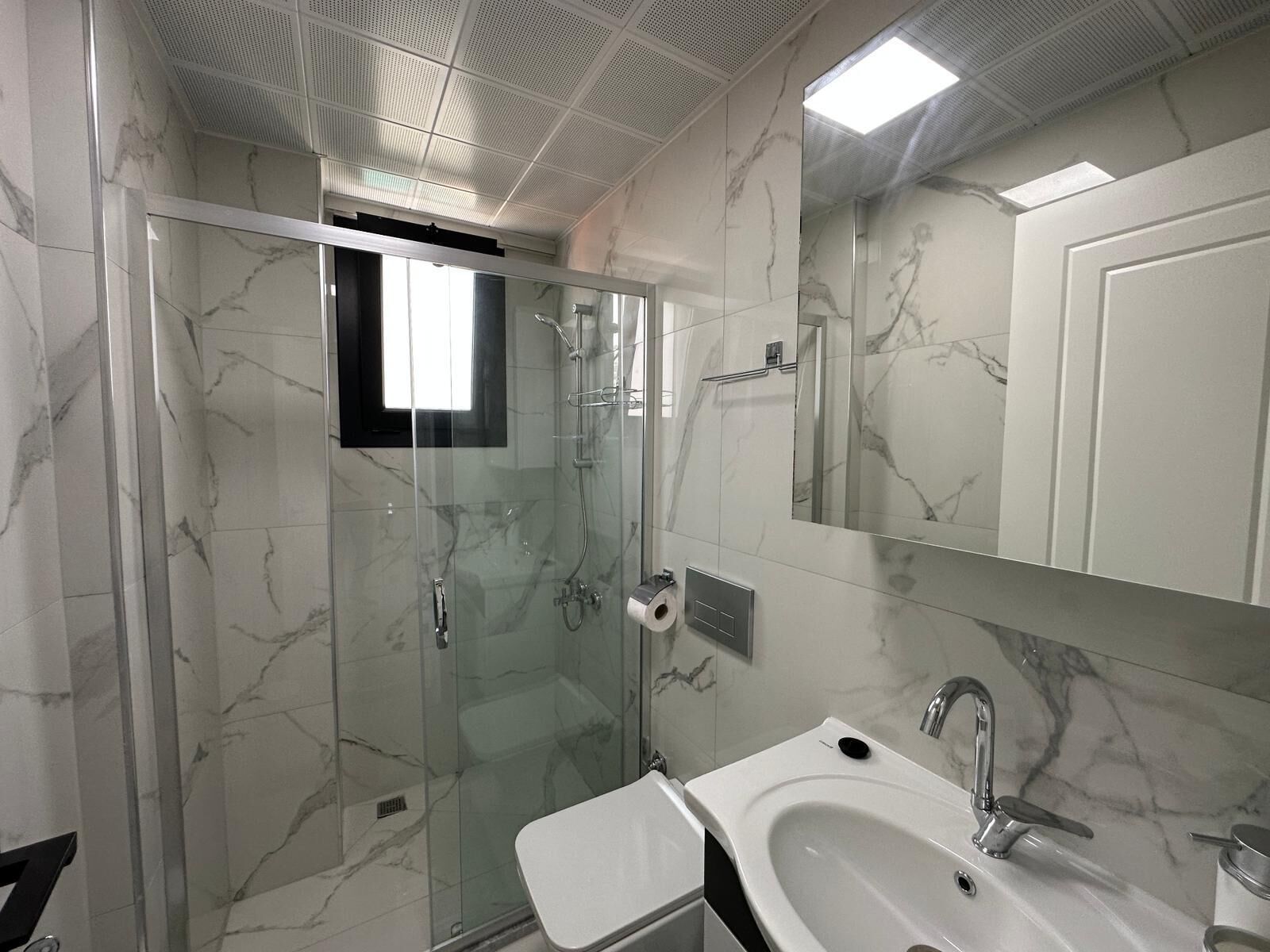 A modern bathroom with a glass-enclosed shower, a white sink, and a large mirror.