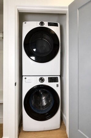 A compact, white stacked washer and dryer unit in a narrow space. - Cozy 1BR Apartment in Atlanta – Prime Location Near Midtown & Downtown (Atlanta)