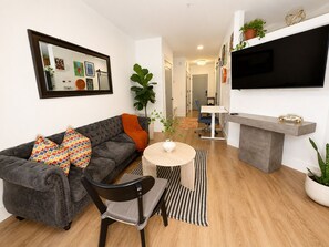 A modern living room with a grey sofa, a round wooden coffee table, a black chair, a TV mounted on the wall, and a fireplace. - Cozy 1BR Apartment in Atlanta – Prime Location Near Midtown & Downtown (Atlanta)