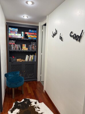 Een hal met een boekenplank, een blauwe stoel, een koeienhuidtapijt en een muur met de tekst 'Just be cool'.