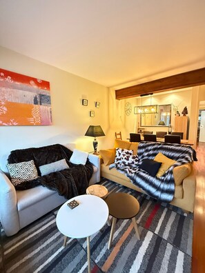 Een woonkamer met een bank, een bijzettafeltje en een eethoek met stoelen en een tafel.