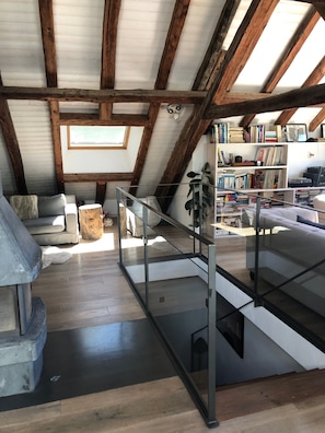 Un espacio tipo loft con vigas de madera a la vista, una escalera de cristal, una estantería y una chimenea.