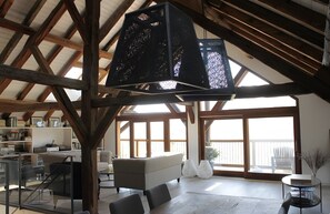 Un loft espacioso con techos altos, vigas de madera a la vista, un ventanal grande y una zona de estar acogedora.