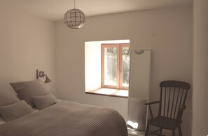 Ein Schlafzimmer mit einem Bett, einem Sessel, einem Fenster und einer Pendelleuchte.