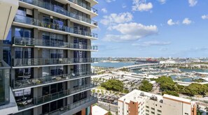 Un edificio de varios pisos con balcones, un puerto deportivo con barcos y un cielo despejado.