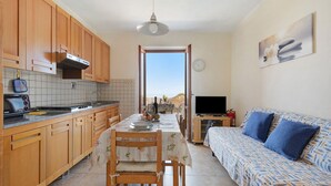 Una cocina con armarios de madera, una mesa de comedor con sillas, un sofá, un televisor y una vista a través de una puerta.