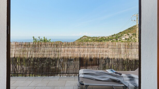 Un balcón con vista al mar, una cerca de madera y una silla de lounge con un libro y gafas de sol.