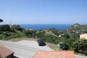 Une route côtière avec une voiture garée, des maisons et une vue dégagée sur la mer.