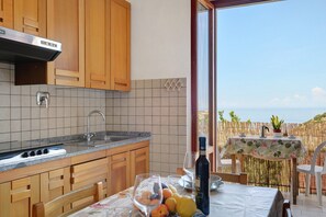 Una cocina con armarios de madera, una campana extractora de acero inoxidable y vistas al mar a través de un ventanal grande.