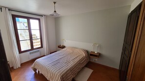 Ein Schlafzimmer mit Bett, Fenster, Heizkörper, Deckenventilator und einem Holzschrank.