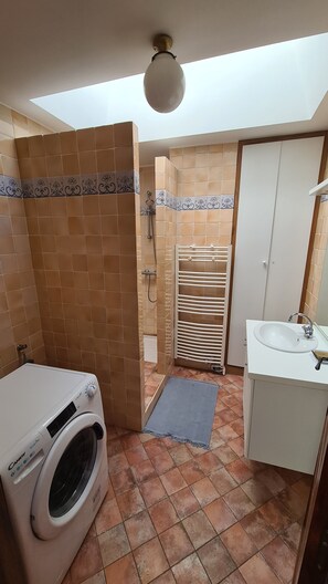 Une salle de bain équipée d’un lave-linge, d’une douche, d’un porte-serviettes et d’un lavabo.