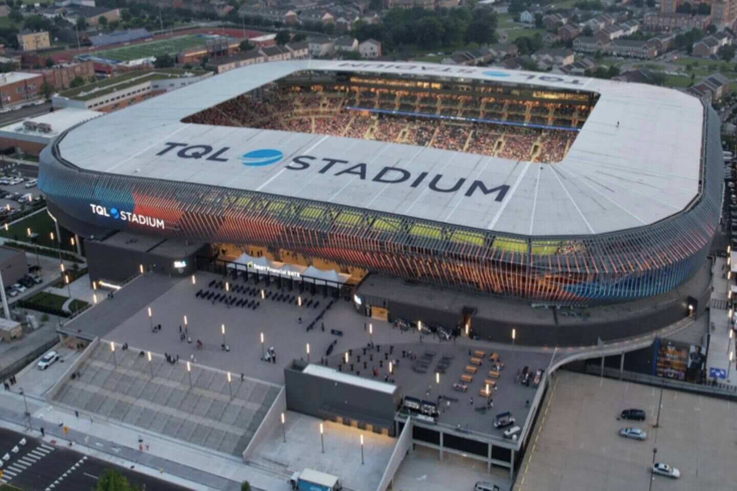 Ein großes Stadion, auf dessen Dach 'TQL Stadium' steht, umgeben von Parkplätzen und einem überdachten Bereich.