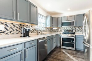 Eine moderne Küche mit grauen Schränken, einem Edelstahlkühlschrank, einem eingebauten Backofen und einer Kaffeemaschine.