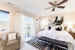 Ein Schlafzimmer mit einem großen Bett, einem Deckenventilator, Blick durch das Fenster und einer Stadtlandschaft draußen.