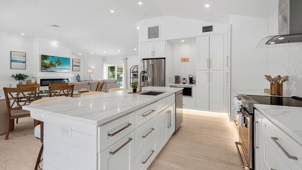 Cocina moderna con armarios blancos, una isla grande, electrodomésticos de acero inoxidable y un comedor con sillas de madera.