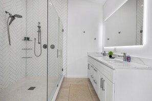 Une salle de bain moderne avec une douche à parois de verre, un meuble-lavabo blanc avec un miroir et une petite plante en pot posée sur le plan de travail.