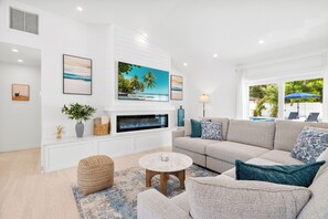 Ein modernes Wohnzimmer mit Kamin, einer großen Couch, einem runden Couchtisch und Blick ins Freie.