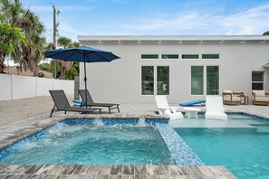 Ein Swimmingpool mit Liegestühlen, einem blauen Sonnenschirm und einem modernen Haus im Hintergrund.